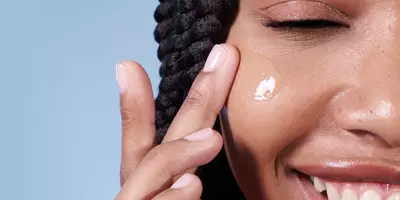 Woman smiling while applying hydrating serum to dry winter skin