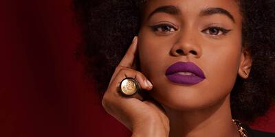 Dark purple lipstick in a matte finish worn on a dark skin tone.