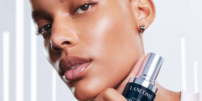 Woman with a dark skin tone holding up a bottle of Advanced Genifique Face Serum for a healthy skin moisture barrier