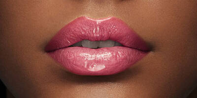 Woman with a dark skin tone wearing a glossy bright pink lip color with a metallic shimmer finish.