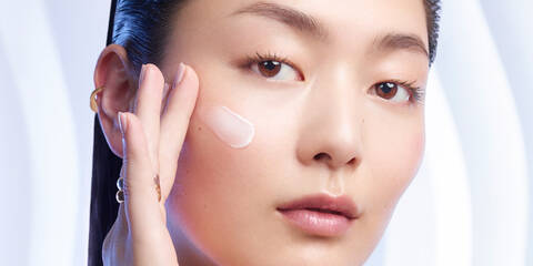 Asian woman applying moisturizer to her cheek