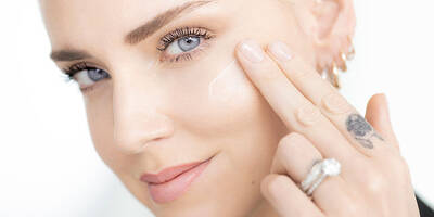 Woman applying anti-wrinkle face cream to her skin using fingertips.