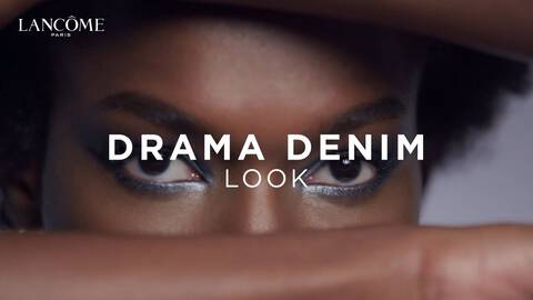 Woman showing how to create a drama denim inspired eye makeup and eyeshadow look on dark skin.