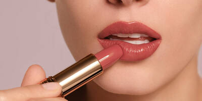 Woman applying creamy nude lipstick shade onto fair skin