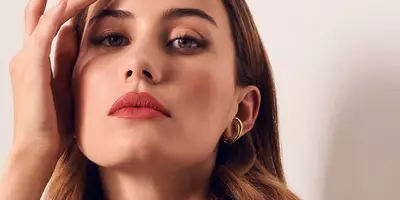 Woman applying lipstick as blush to create a monochromatic pink makeup look