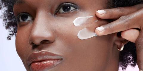 Black woman with dark skin tone applying sunscreen on cheek