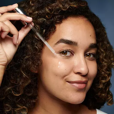 Young woman dispensing hyaluronic acid for face serum from a pipette onto her cheek
