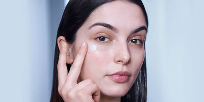 Woman applying Lancome’s Genifique hydrating eye cream to dry skin around eyes