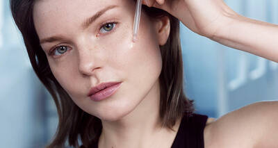Woman applying Advanced Genifique face serum with a dropper
