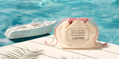 Tan makeup bag on a dock holding travel size toiletries from Lancome with a toy speed boat in the water