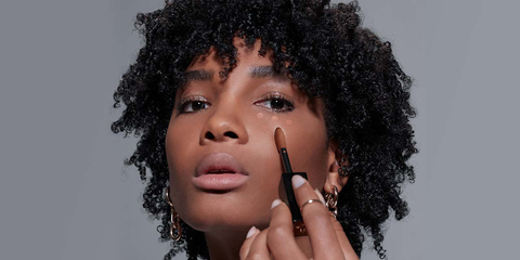 Woman with dark skin tone showing how to apply all over concealer under the eyes.