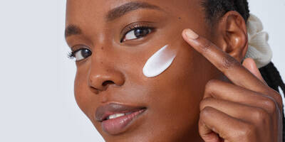 Woman with dark skin applying moisturizer to dry skin