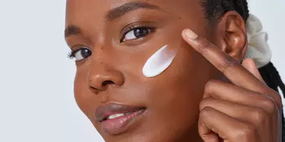 Woman applying one of Lancome’s  best moisturizers for dry skin to her cheek