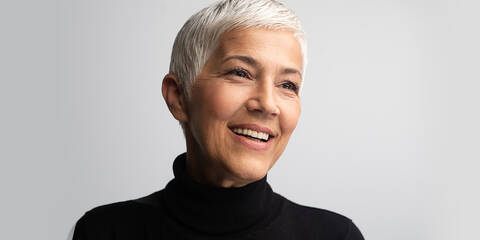 Mature woman with short white hair wearing a black turtleneck and smiling