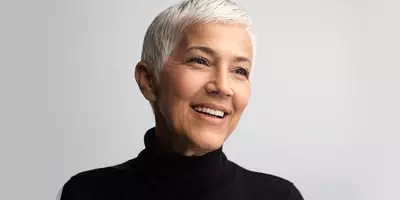 Mature woman with short white hair wearing a black turtleneck and smiling
