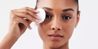 Woman with dark skin removing eye makeup with a cotton round pad and bi-facil eye makeup remover