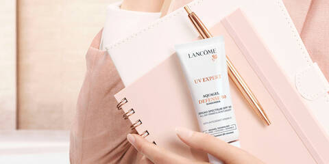 Woman wearing all pink holding a pink planner, notebook, pen and a tube of UV Expert Aquagel Defense SPF 50 sunscreen
