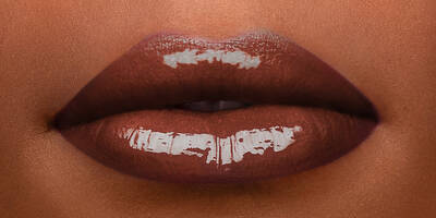 Dark chocolate brown lip gloss in an 80s shade worn on a model with dark skin