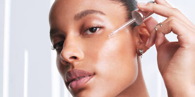 Woman with dark skin applying a hydrating hyaluronic acid serum to help with the skin moisture barrier and glow