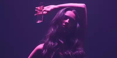 Olivia Rodrigo with long flowy hair under pink light holding Idole Power eau de parfum Intense