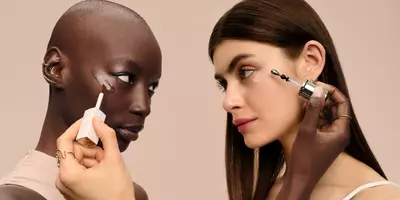 Two women applying concealer under eyes and illuminating serum on each other to conceal and brighten dark circles