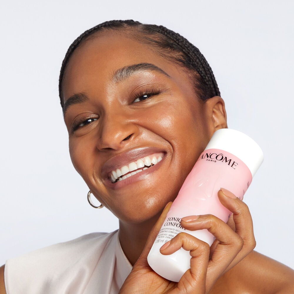 Model smiling while holding up Tonique Confort Hyaluronic Acid Milky Toner 