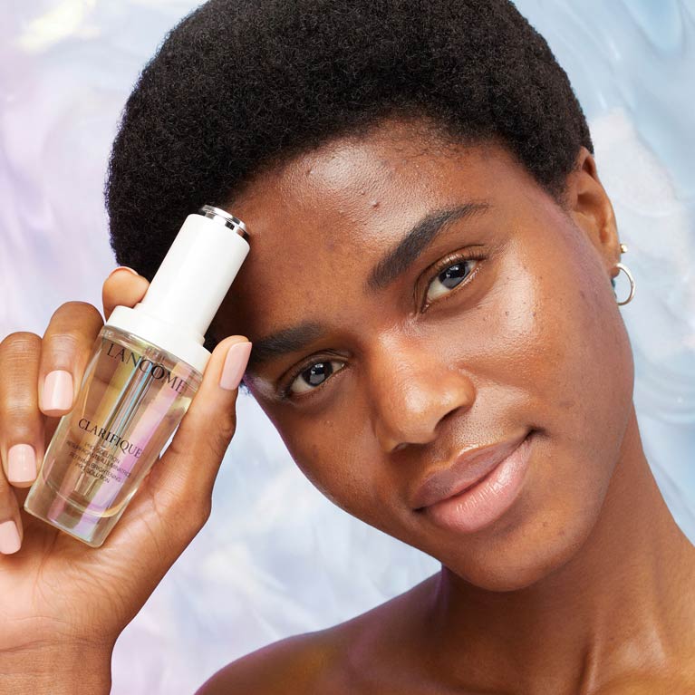Woman with a dark skin tone and dark spots holding a brightening serum 