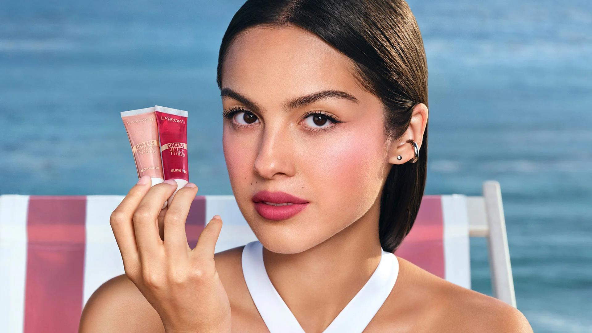 Model holding two Lancôme Juicy Tubes by the sea.